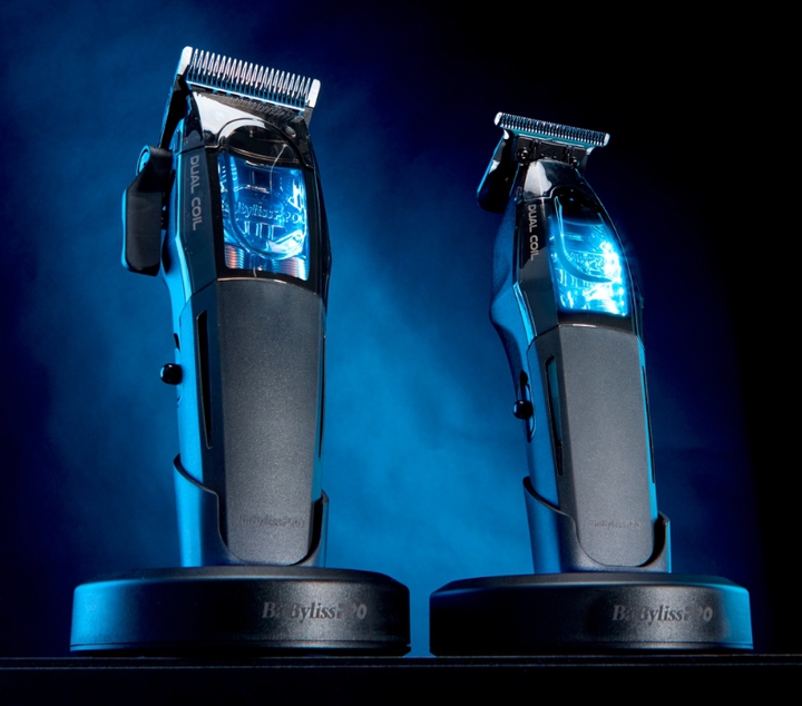 BaBylissPRO barber clipper and trimmer in an upright position on charging stands, illuminated by blue light against a dark background.