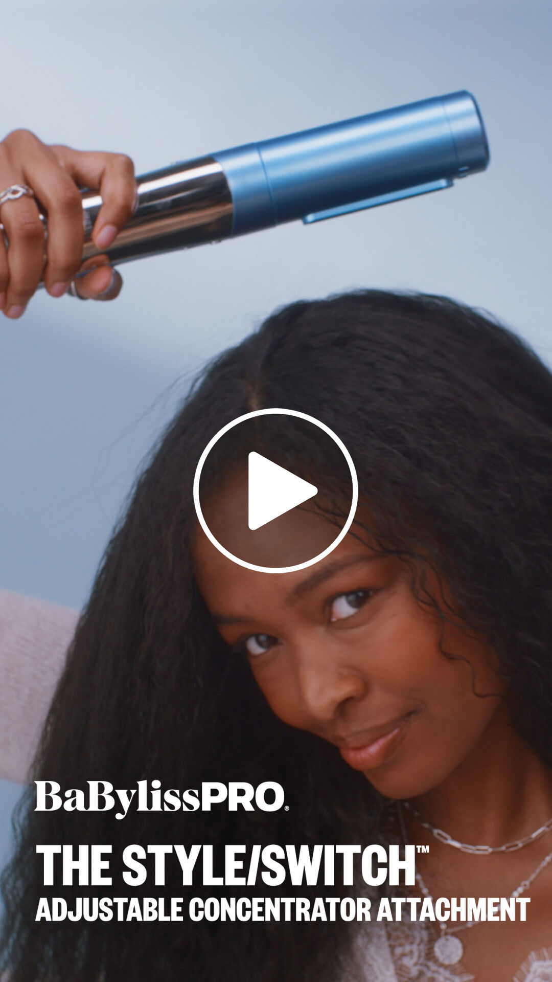 A woman with black wavy hair using a BaBylissPRO adjustable concentrator attachment to blow dry her hair with the style switch multi styler hair tool